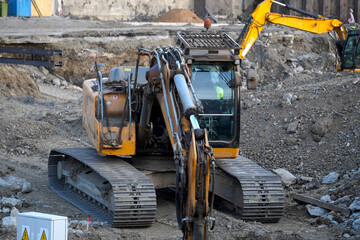 Vertical shot of a heavy yellow crawler excavator operating in a pit at an urban construction and excavation site. © VladyslavShcherbakov