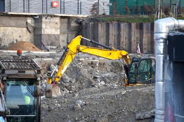 Vertical shot of a heavy yellow crawler excavator operating in a pit at an urban construction and excavation site. © VladyslavShcherbakov