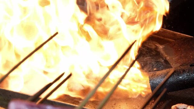Whole grilled squid skewers cooking on hot flaming grill with smoke. Street food vendor grilling fresh seafood on barbecue plate.