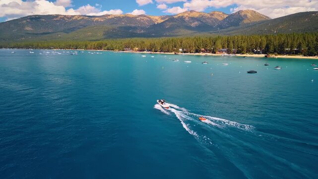 Motorboat towing a tube near the shore of Lake Tahoe. A white boat pulls an orange float across blue water, with anchored vessels below wooded mountains.