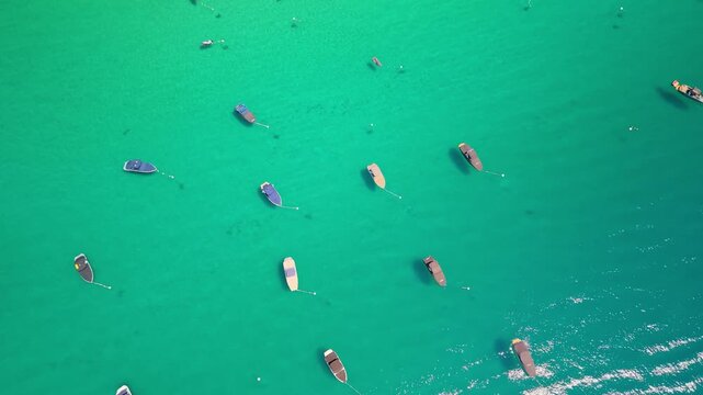 Overhead view of moored boats on green Lake Tahoe water. Small vessels sit beside white buoys, with faint underwater shadows and a patch of surface glare.