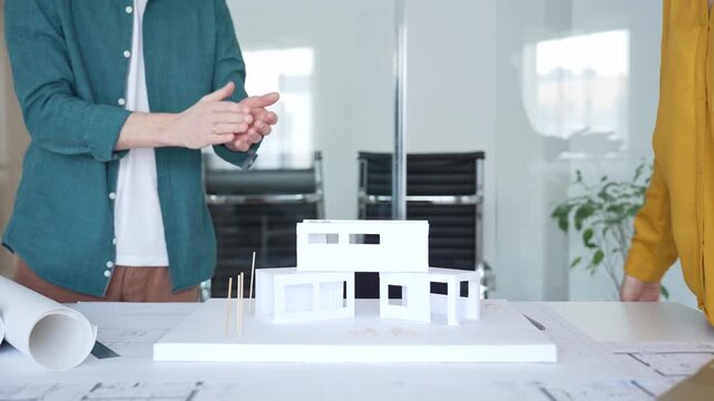 Business partners shaking hands over architectural model, finalizing real estate deal during office meeting. Architecture and business concept