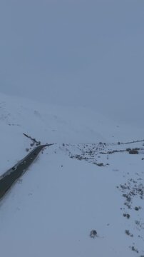 Drone view of a mountain highway crossing Ala-Bel Pass with cars driving through a vast snowy landscape, high-altitude valley and ridges in Kyrgyzstan