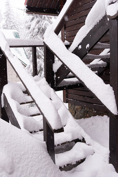 Snow covered wooden outdoor staircase and railing in a residential yard after heavy winter snowfall, rustic architecture, deep fresh snow, cold weather and peaceful seasonal atmosphere outdoors