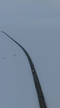 Drone footage of a lonely asphalt road cutting through vast snowfields at Ala-Bel Pass, high in the Tien Shan mountains of Kyrgyzstan, cold winter landscape