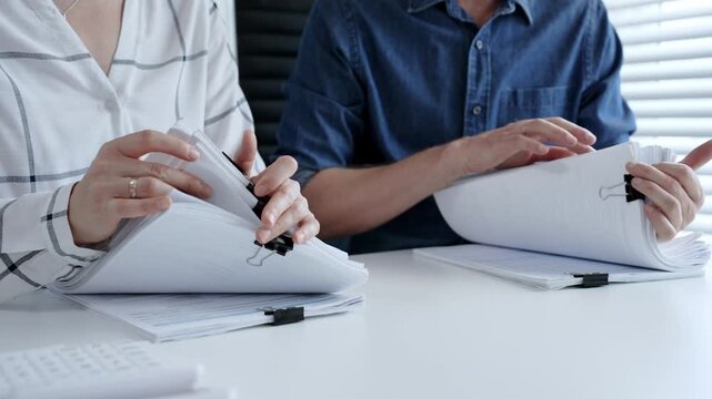 Colleagues reviewing financial data, examining documents, and organizing files with binder clips in an office, managing business paperwork and accounting workload