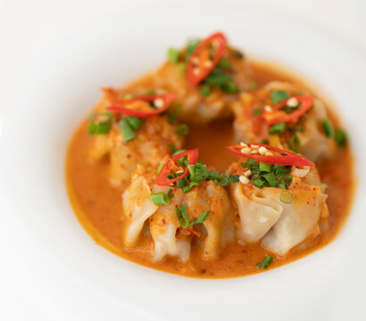 Delicious dumplings served in a bowl with a spicy sauce and green onions, savor rich, steaming dumplings soup, culinary dumplings delight, Dumplings coated in a spicy red-orange sauce