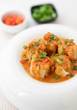 Delicious dumplings served in a bowl with a spicy sauce and green onions, savor rich, steaming dumplings soup, culinary dumplings delight, Dumplings coated in a spicy red-orange sauce