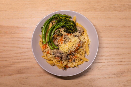 A plate of sausage pasta with broccolini and cheese.