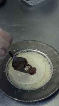 A spoon releases thick chocolate spread over a pale creamy layer in a round kunafa pan.