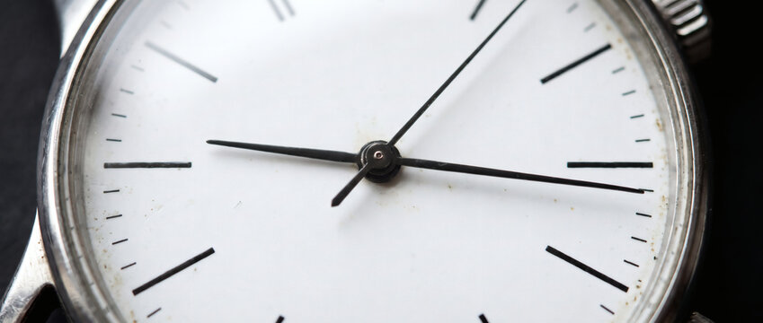 A close-up shot of a minimalist wristwatch dial with black hands and white face, showing timekeeping components clearly.