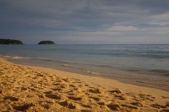 Tropical secluded beach with golden sand, scenic green hill and ocean waves under blue sky
