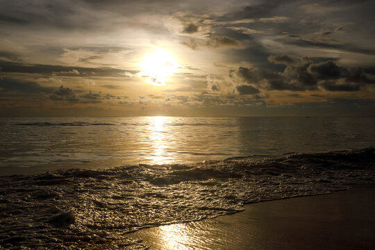 Golden sunset over the sea with sun breaking through clouds and glittering reflection on ocean water
