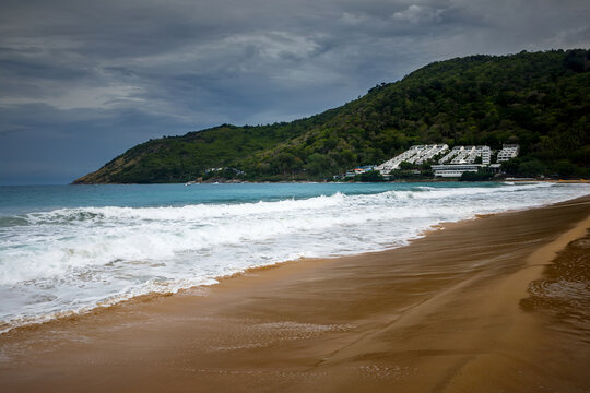 Tropical secluded beach with golden sand, scenic green hill and ocean waves under blue sky