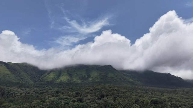 Dramatic White Clouds Rolling Over Lush Green Mountain Ridge Under Bright Blue Sky