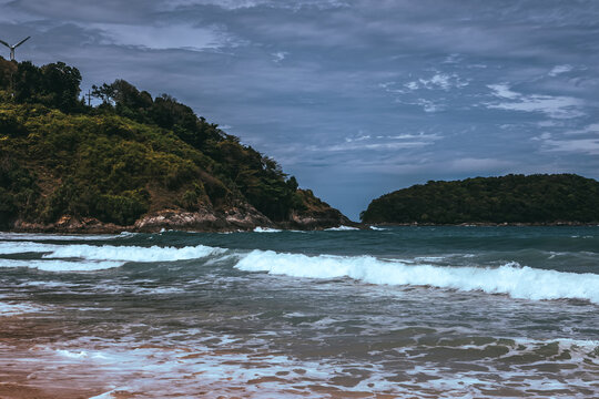 Tropical secluded beach with golden sand, scenic green hill and ocean waves under blue sky