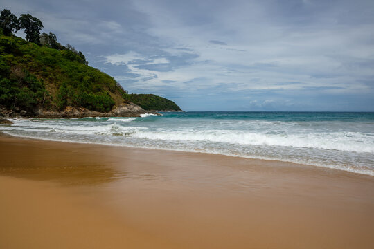 Tropical secluded beach with golden sand, scenic green hill and ocean waves under blue sky