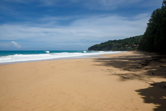 Tropical secluded beach with golden sand, scenic green hill and ocean waves under blue sky