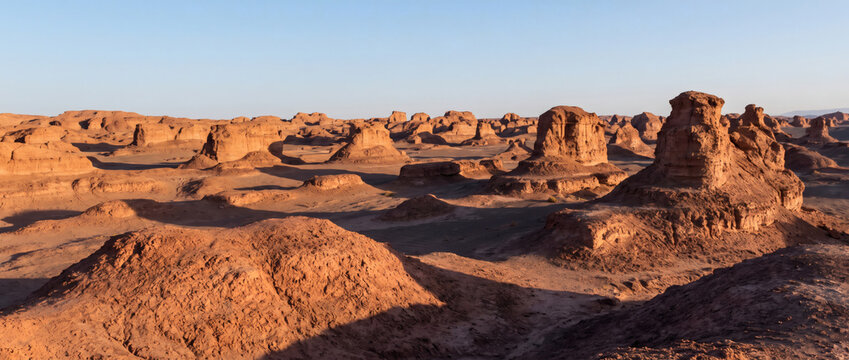 This landscape shows eroded rock formations shaped by wind and water in a vast, arid desert under a clear sky.