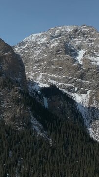 Aerial footage of rugged peaks, snow patches and dense conifer forest on steep mountain slopes in Barskoon Gorge, Issyk Kul Region, Kyrgyzstan