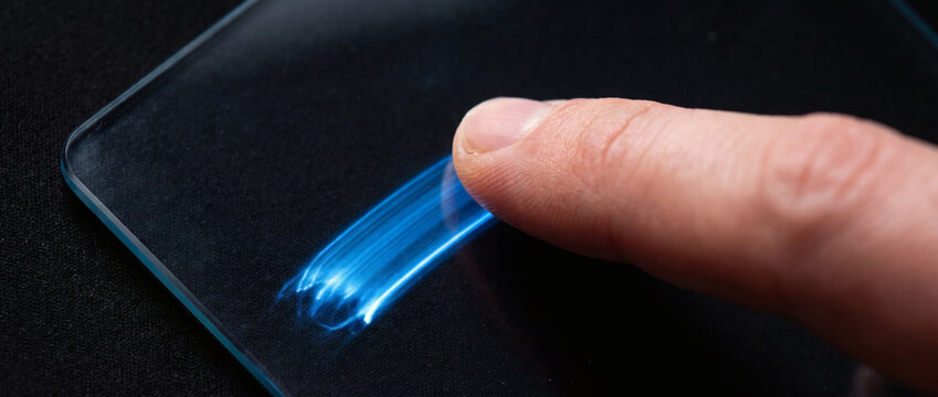 A human finger touches a touchscreen, triggering a glowing blue light effect on the device surface.