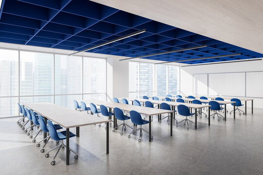 Modern blue and white classroom interior with rows of desks, rolling chairs, expansive windows, and geometric ceiling lighting design. 3D Rendering