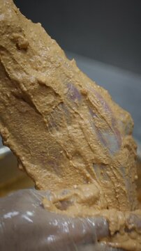 A gloved hand rubs thick seasoning paste over a large bone in meat cut before turning it above a tray.