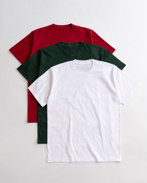 Flat lay of blank white green and red cotton t shirts layered on a light background for apparel mockup design