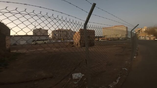 Tracking shot of fenced ancient stone ruins and modern city buildings at dusk in Medina.