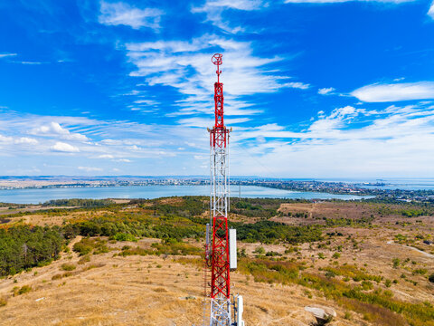Telecommunication tower stands tall over a landscape with a city view and blue skies with clouds in the background