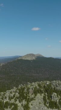 Drone footage of a rocky mountain ridge above dense taiga forest under a clear blue sky in Taganay National Park, Chelyabinsk Oblast, Russia