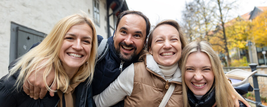 Cheerful friends laugh together on autumn city walk, sharing hugs and joyful travel moments. Candid group portrait captures friendship, reunion, happiness, leisure and weekend adventure outdoors