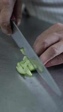 A cook slices through cucumber rounds with a large kitchen knife to make smaller pieces for food preparation.