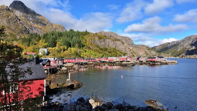 Traditional red wooden houses line the small harbor of Nusfjord in the Lofoten Islands, surrounded by rocky mountains and greenery.