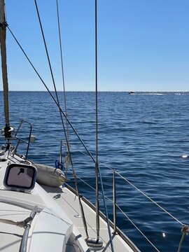 View from the deck of a sailboat looking out at the open blue sea and distant coastline.