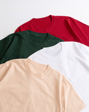 A top down flat lay view of a collection of folded colorful cotton t shirts including red green white and nude arranged neatly on a clean white background