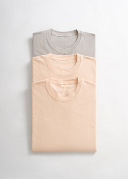 A stack of neatly folded pastel colored cotton t shirts in neutral shades on a white background