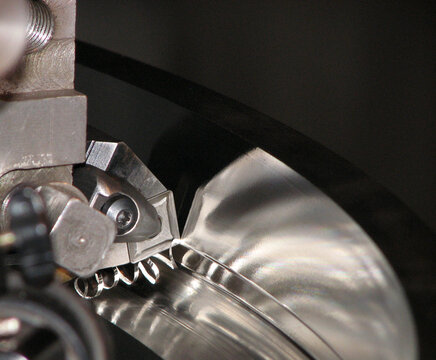 Extreme close-up of an indexable carbide insert cutting tool machining a steel workpiece on a lathe, producing spiral metal swarf chips in a precision metalworking operation.
