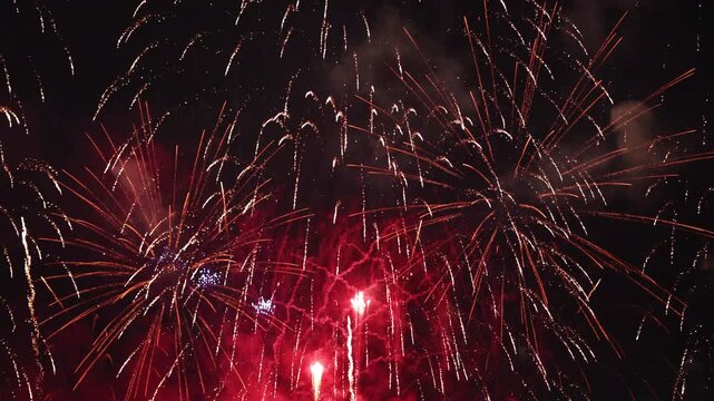 Colorful fireworks exploding with red and gold sparks over dark night sky, bright pyrotechnics celebration show, holiday festival, New Year eve, anniversary party, and event concept