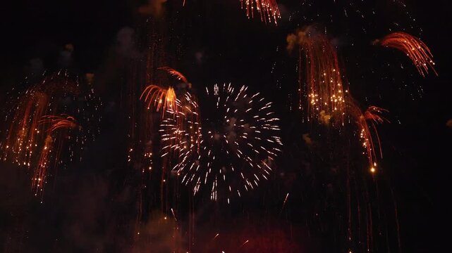 Colorful fireworks exploding with red and gold sparks over dark night sky, bright pyrotechnics celebration show, holiday festival, New Year eve, anniversary party, and event concept