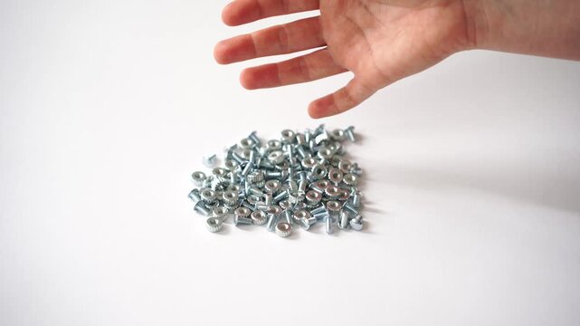 Close up of a human hand pouring metal screws onto a surface, ideal for DIY, home repair, construction projects and mechanical maintenance visual themes