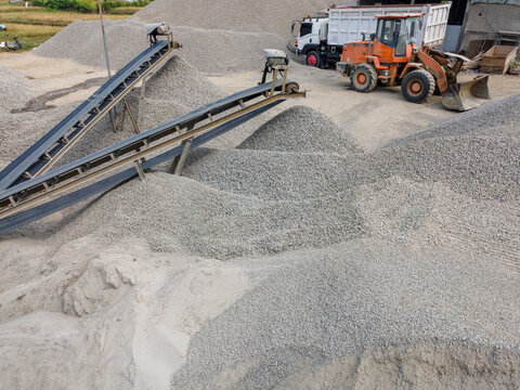 Heavy Machinery Orange Wheel Loader Near a Rock Crusher Machine with Conveyor Belt System and Aggregate Stockpiles Viewed from Above in Banyumas, Central Java, Indonesia.