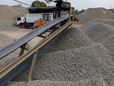 Heavy Machinery Orange Wheel Loader Near a Rock Crusher Machine with Conveyor Belt System and Aggregate Stockpiles Viewed from Above in Banyumas, Central Java, Indonesia.