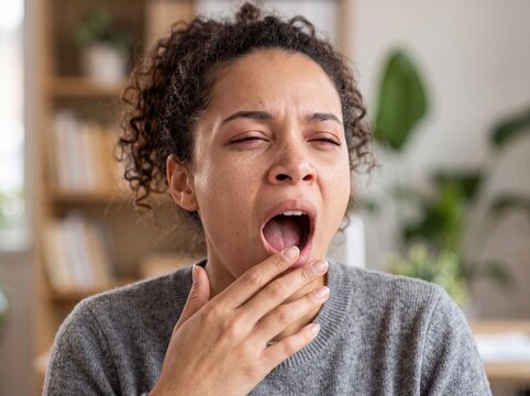 Tired young woman with curly hair yawning and covering her mouth