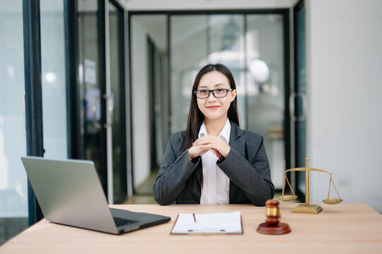 Asian female lawyer in a suit and glasses sitting at her modern office desk. Professional attorney providing trusted legal advice