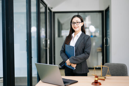Asian female lawyer in a suit holding a contract in her office. Confident attorney standing by a desk