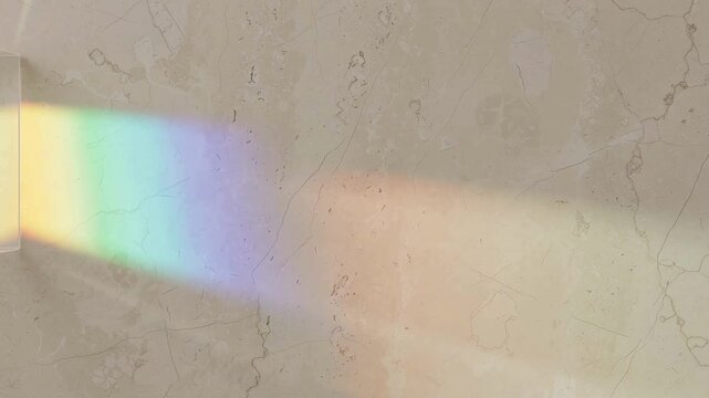 A vibrant rainbow light prism reflection cast upon a textured beige marble wall surface.
