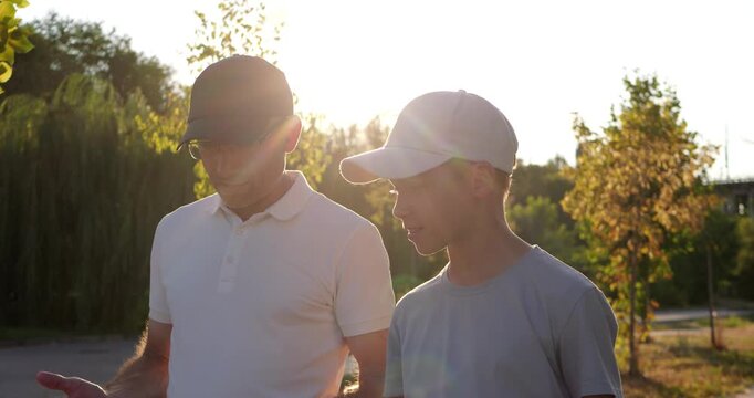 Dad and son walk and talk together in sunny park. They share conversation during peaceful evening stroll outdoors. Family bonding supports parenting, connection, and happy outdoor lifestyle themes.