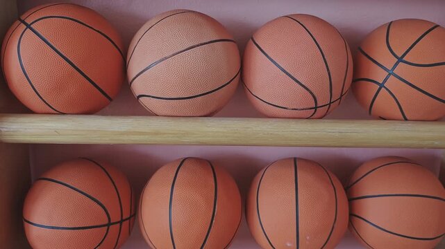 Rows of new basketballs neatly arranged on wooden shelves. Sports equipment for team games, training, and physical education class