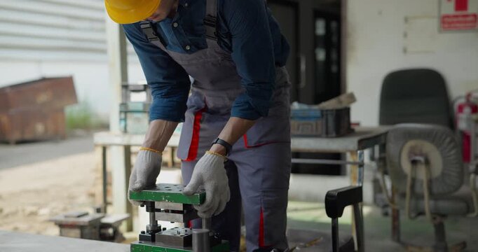Factory worker in hard hat using tools to file metal part in bench vise at workshop